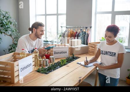 Junge Mädchen schreiben, Mann mit Tablett arbeitet in Freiwilligenorganisation. Stockfoto