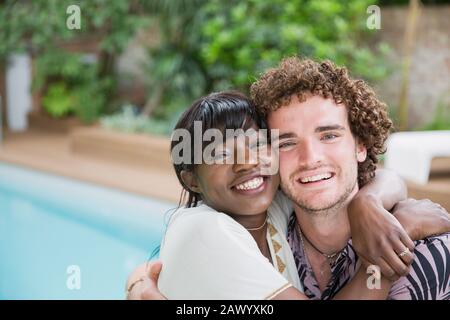 Portrait fröhliches junges, multiethnisches Paar, das sich am Pool umarmt Stockfoto
