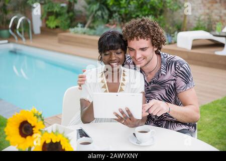 Glückliches multiethnisches Paar mit digitalem Tablet auf der Terrasse am Pool Stockfoto