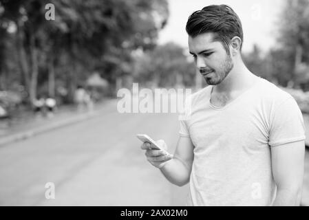 Profilansicht des jungen gutaussehenden Mannes mit dem Telefon im Park Stockfoto