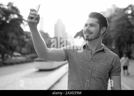 Porträt eines fröhlichen jungen gutaussehenden Mannes, der selfie im Park mitnimmt Stockfoto