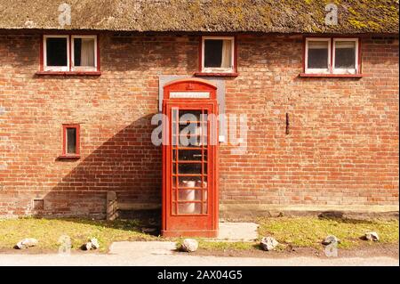 Rote Telefonzelle in der Nähe einer Backsteinmauer mit Fenstern Stockfoto