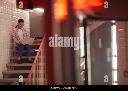 Weitwinkelporträt moderner Asiaten mit Laptop beim Sitzen auf der Treppe, Kopierraum Stockfoto