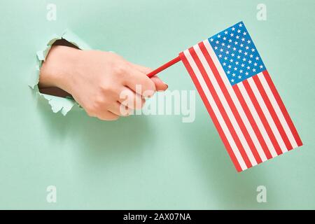 Eine Hand aus einem Loch in Grünpapier hält eine amerikanische Flagge mit blauen Sternen. America Independence Day Konzept. Kopierbereich Stockfoto