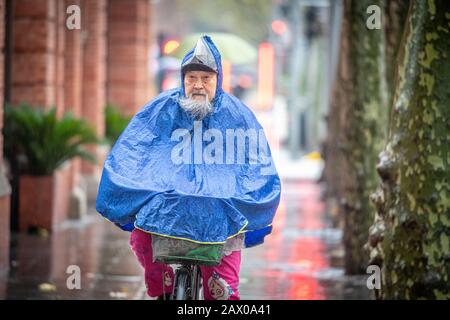 Ein entschlossener älterer Mann fährt mit seinem Fahrrad im Regen, Shanghai, China. Stockfoto