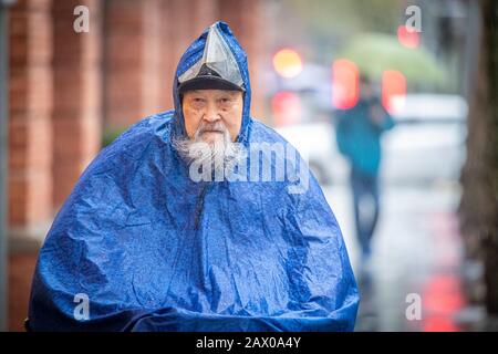 Ein entschlossener älterer Mann fährt mit seinem Fahrrad im Regen, Shanghai, China. Stockfoto