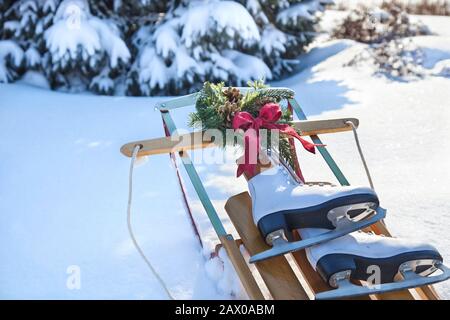 Vintage-Schlitten im Schnee mit Kranz und roter Schleife und weißen Schlittschuhen am sonnigen Tag Stockfoto