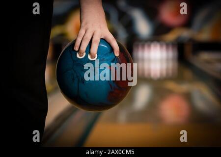 Zehn-Pin-Bowling-Ball in Handnähe gehalten, mit Bowlingbahn und Pins Hintergrund Stockfoto