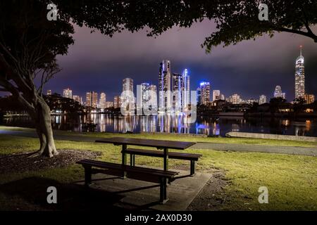 Parkbank mit Skyline der Stadt Surfers Paradise auf dämmerungsfarbenem Hintergrund, Gold Coast, Australien Stockfoto