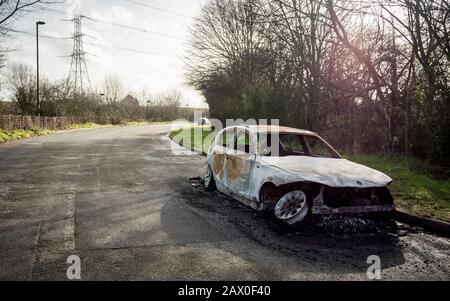 Ein abgebranntes Auto blieb auf der Straßenseite einer ruhigen ländlichen Lage stehen. Stockfoto