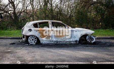 Ein abgebranntes Auto blieb auf der Straßenseite einer ruhigen ländlichen Lage stehen. Stockfoto