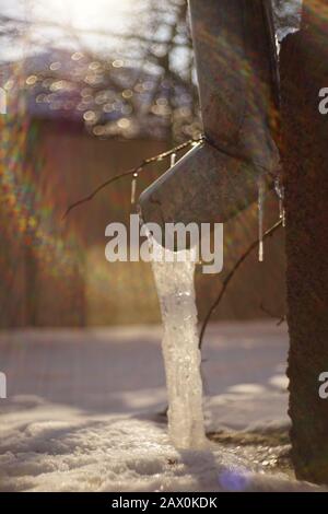 Drainpipe an der Hausecke mit Eis und Sonnenlicht. Verschwommen Stockfoto