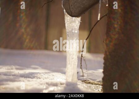 Drainpipe an der Hausecke mit Eis und Sonnenstrahlen Stockfoto