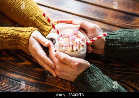 Ein Paar hält die Hände um eine Tasse heißen Schokoladenkakaos mit herzförmigem Marshmallow als Belag Stockfoto