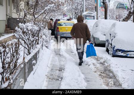 Bukarest, Rumänien - 6. Februar 2020: Bukarest Bürgersteig im Winter mit illegal abgestellten Autos, mit Schnee bedeckt, und einem gelben Dacia Auto, das pe blockiert Stockfoto