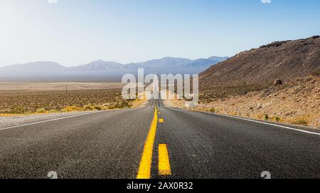 Schöner Panoramablick auf die lange gerade Straße, die sich durch eine karge Landschaft des wilden amerikanischen Südwestens mit Hitzehaltung an einem sonnigen Tag im Sommer schneidet Stockfoto