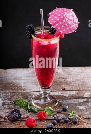 Cocktail aus Waldfrüchten in einem Glas auf einem Holzsockel, der mit Brombeeren verziert ist Stockfoto