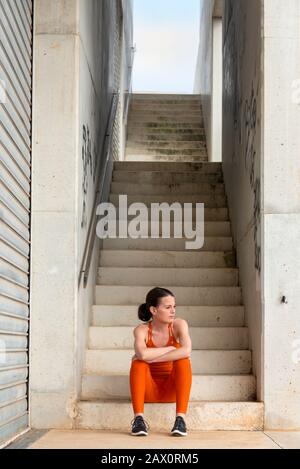 Weibliche Athletin, die sich nach dem körperlichen Training ausruhen kann. Auf Betonstufen sitzend, urbanes Ambiente. Stockfoto