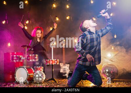 Kinder geben vor, eine Rockband zu sein und im Studio oder auf der Bühne zu singen. Junge singen und Mädchen zahlen am Schlagzeug Stockfoto