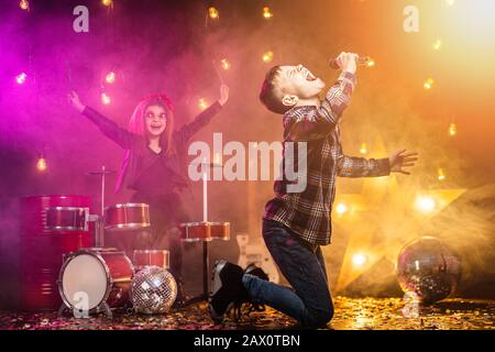 Kinder geben vor, eine Rockband zu sein und im Studio oder auf der Bühne zu singen. Junge singen und Mädchen zahlen am Schlagzeug Stockfoto