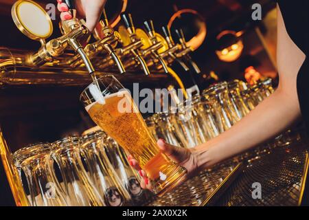 Nahaufnahme eines männlichen Barkeeders, das Fassbier in einem Pub abfüllt, der einen großen Glaskard unter einem Zapfenaufsatz auf einem Edelstahl hält Stockfoto