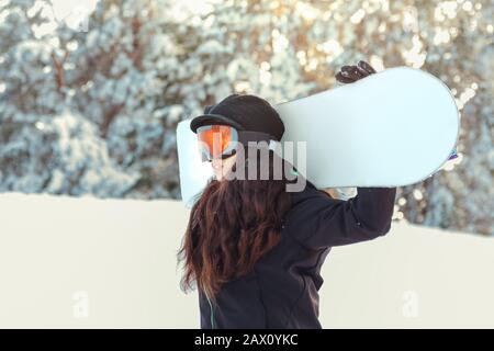 Stock-Foto eines jungen Mädchens, das ihr Snowboard auf einem verschneiten Berg hält Stockfoto