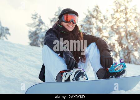 Stock-Foto eines jungen Snowboarders lächelt und sitzt auf dem Schnee des Berges Stockfoto