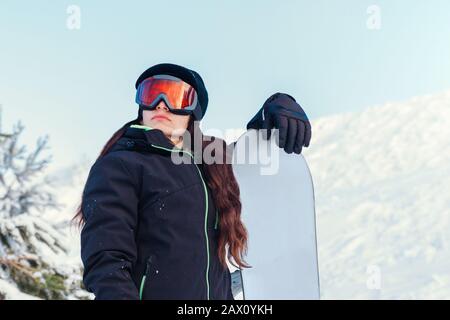 Stock-Foto eines jungen Mädchens, das ihr Snowboard auf einem verschneiten Berg hält Stockfoto