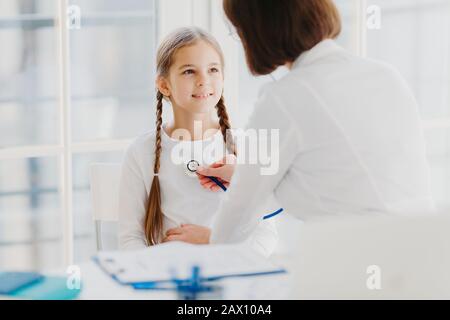 Hausarzt untersucht Kind, hört Lungen mit Stethoskop, stellt Rezeptposieren im Krankenhaus vor. Das kranke Kind hat Kälte, kommt Stockfoto