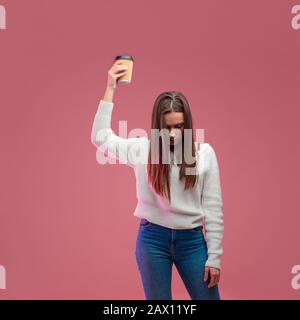 Ich brauche mehr Kaffee. Schläfrige Studentin schläft im stehen und will aufheitern, nachdem sie eine zweite Portion Kaffee erhalten hat. Rosafarbener Hintergrund. Stockfoto