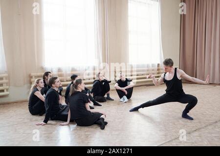 Gutaussehender Choreograf, der zeitgenössische Tanzbewegungen in seinem jungen Team demonstriert Stockfoto