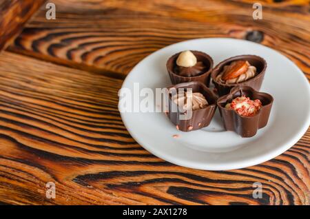 Schokoladenkäuze auf einer weißen Untertasse. Nahaufnahme von vier leckeren Süßigkeiten auf einem Holztisch. Süßwaren. Seitenansicht. Selektiver Fokus. Stockfoto