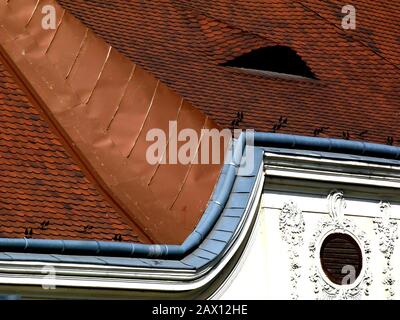 Kupferblitzdetails und Tonfliesen, Dormer, ovales Fenster, mit Rokoko dekorierte stuckierte Erhöhung. Alte architektonische Details in Budapest, Ungarn. Stockfoto