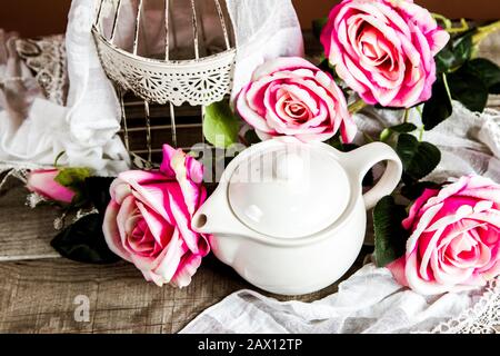 Weißer Käfig und eine Teekanne mit Rosen und Dekoration auf einem Holztisch Stockfoto