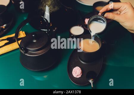 Frau, die Milch in einem Becher Tee aus dem Wasserkocher gießt Stockfoto