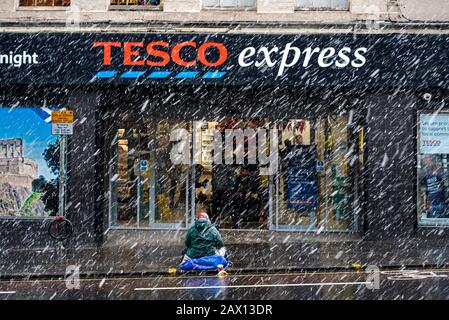 Obdachlose oder Bettler sitzt bettelnd während eines blizzards vor dem Tesco Express-Laden in der Nicolson Street, Edinburgh, Schottland, Großbritannien. Stockfoto