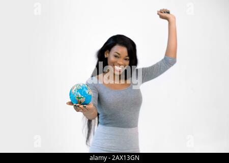 Halblingenporträt des aufgeregten afrikanischen Mädchens in grauem Kleid, das eine Hand hält, Erdweltkugel hält und isoliert auf weißem Hintergrund in Su steht Stockfoto