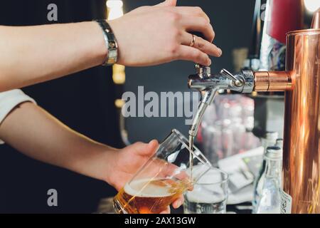 Nahaufnahme eines männlichen Barkeeper abfüllen Bier in einem Pub mit einem großen Glas Krug unter einem Zapfen Anlage auf einem Edelstahl Fass. Stockfoto