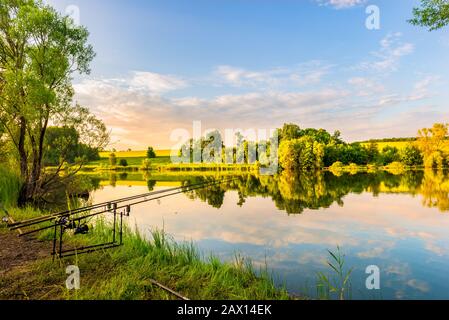 Angelruten an einem Ufer des ruhigen Flusses bei Sonnenuntergang Stockfoto