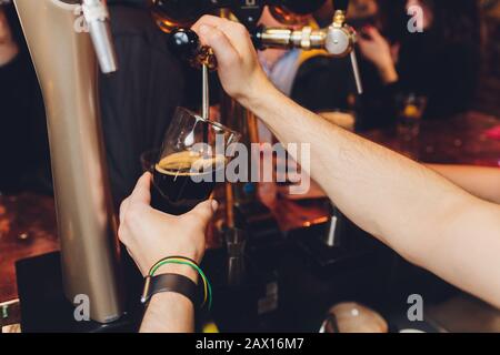 Nahaufnahme eines männlichen Barkeeper abfüllen Bier in einem Pub mit einem großen Glas Krug unter einem Zapfen Anlage auf einem Edelstahl Fass Stockfoto