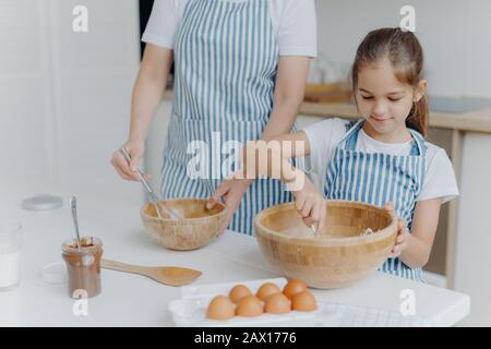 Mutter erteilt Kleinkind kulinarische Lektion, steht nebeneinander, mischt Zutat in große Holzschüsseln, macht Teig zusammen, verwendet Eier, Mehl und o Stockfoto