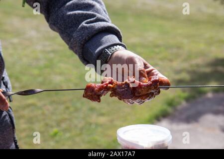 Die Hände eines Mannes, der das Fleisch am Spieß für Grill. Nahaufnahme der nicht gegartem Fleisch am Spieß. Stockfoto