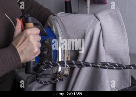 Näherungsmeister, in einem Nähsalon, mit einem Eisen, die Kleidung des Meisters. Der Arbeitsvorgang, bei dem Kleidung, einschließlich Bügeln, für die nachfolgende Arbeit gemacht wird Stockfoto