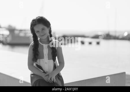 Porträt eines schönen kleinen Mädchens mit langen Haaren in der Nähe des Sees an einem sonnigen Tag. Schwarz und Weiß. Stockfoto