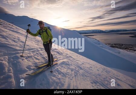 Mann beim Sonnenaufgang auf dem Skisport in Island mit Wasser hinter ihm Stockfoto