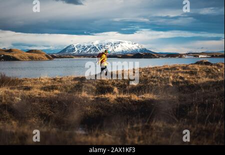 Frau, die durch Feld neben See mit Bergen in der Ferne Stockfoto