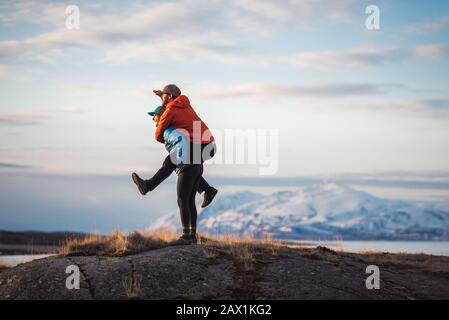 Frau, die Mann Huckepack mit Bergen hinter ihnen Stockfoto