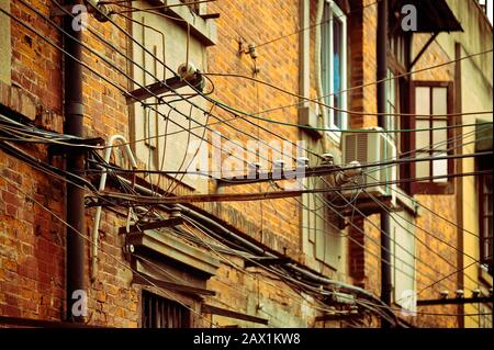 Veraltetes Elektronetz, alte Drähte an der Fassade des Ziegelbaus befestigt. Shanghai, China. Stockfoto
