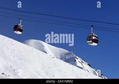 Gondelbahn, schneebedeckte Skipiste, hohe Winterberge und blauer klarer Himmel an sonnigen Tagen. Kaukasusgebirge. Georgien, Region Gudauri. Stockfoto