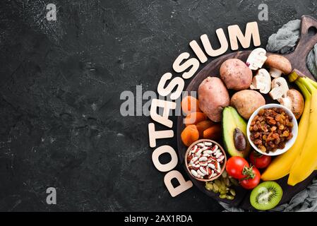 Die Nahrung enthält natürliches Kalium. K: Kartoffeln, Pilze, Banane, Tomaten, Nüsse, Bohnen, Brokkoli, Avocados. Draufsicht. Auf schwarzem Hintergrund. Stockfoto